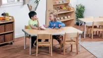 Boy and girl sat at on chairs wooden table in nursery eating grapes