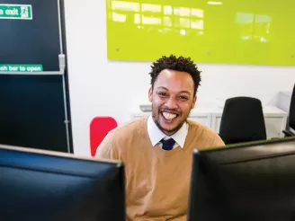 Man smiling and looking at the camera whilst sat at his desk