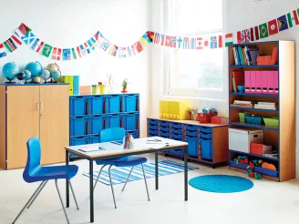 Wooden bookcases, storage cupboards, tables and chairs in a nursery with alphabet bunting on the wall.