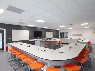 Curved school desk with orange stools in a science lab with wall mounted screen