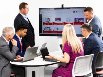 People sat round a meeting room table with Sharp Asset Manager portal on a screen