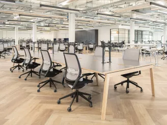 Open plan office environment with wooden flooring and wooden bench desking with task chairs