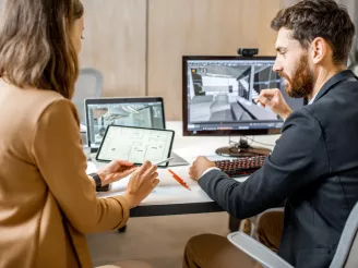 Interior designers sat discussing a project with blueprints on a tablet and designs on computer screen