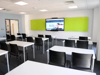 White school desks with black chairs in college classroom with a mounted screen