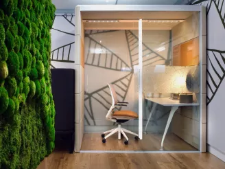 Green living wall with small glass meeting room pod at the end of a corridor with task chair and desk