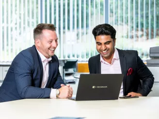 Two business men sat having meeting looking at laptop while smiling