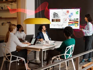 Woman presenting using a Sharp interactive display, team members watching her