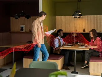 A man and woman working on laptops in a co working booth and a man standing nearby with a tablet