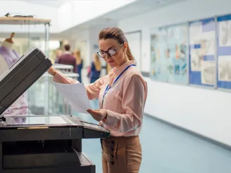 Teacher standing in a hallway looking at a piece of paper whilst holding up the door of a photocopier
