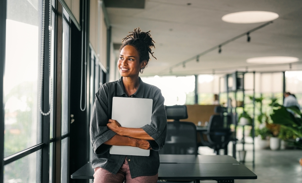 Woman holding laptop in office space, reaping the benefits of Sharp's On-Premise Backup Solutions
